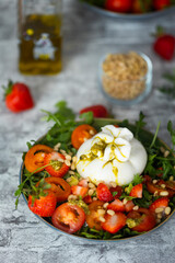 Colorful Italian salad made of arugula leaves, avocado and strawberries slices, pine nuts and burrata cheese with olive oil and pesto sause