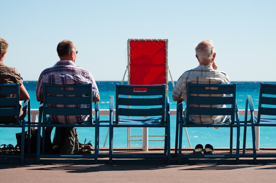 People Sit On Chairs And Look Out To Sea In Nice, France.