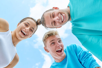 Teenage guys and girl laughing looking down at camera, blue sky background