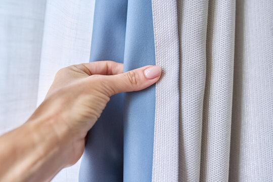 Woman's hand showing light gray curtain on blue opaque lining, fabric blackout