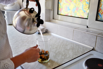 Women's hands brew tea in the kitchen at home. 