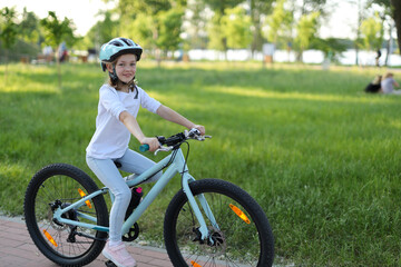 A happy, active young girl biking in the park with a helmet, enjoying a fun and healthy summer...