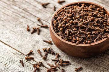 Dry cloves in wooden bowl on rustic table, fresh herb spice concept 