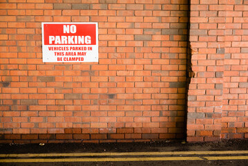 Sign on a brick wall warning that parking is prohibited, and that vehicles parked there may be clamped.
