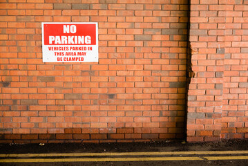 Sign on a brick wall warning that parking is prohibited, and that vehicles parked there may be...