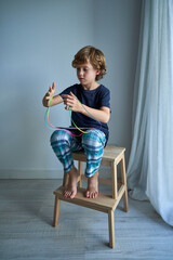 Barefoot boy playing cats cradle game in apartment