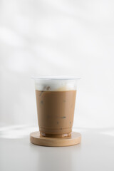 Iced cappuccino in a plastic glass on a white wooden table, minimalist-style picture.