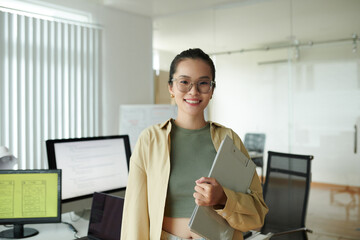 Portrait of positive IT company employee with clipboard standing in office