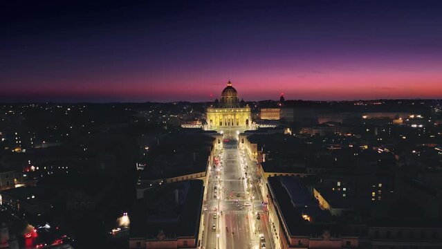 aerial view of rome saint peter basilica vatican city illuminated at night,drone moving out the window flying over conciliazione street at dusk