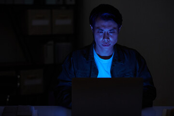 Portrait of serious software developer working on laptop in dark room at night