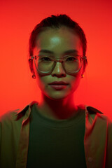 Portrait of young Asian woman in glasses standing in red light