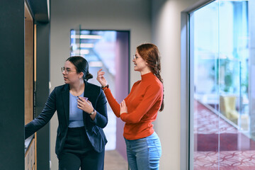 Amidst the contemporary and spacious office setting, two modern young women engage in conversation...