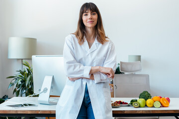 Beautiful smart nutritionist woman working with computer while looking at camera in the nutritionist consultation