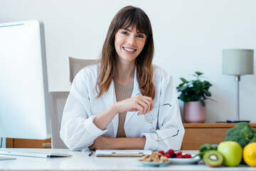 Beautiful smart nutritionist woman working with computer while looking at camera in the nutritionist consultation