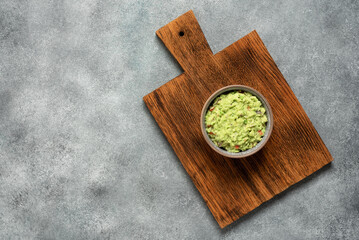 Fototapeta na wymiar Guacamole in a bowl on a wooden board, gray concrete background. Top view, flat lay.