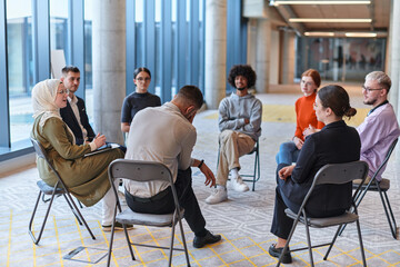 A diverse group of young business entrepreneurs gathered in a circle for a meeting, discussing corporate challenges and innovative solutions within the modern confines of a large corporation