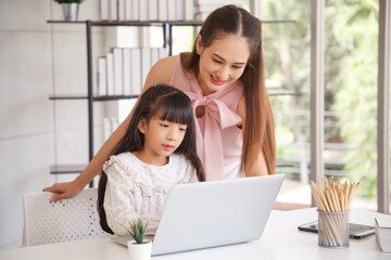 Children education and home school concept : Young asian mother pleased to see little daughters' study online. Excited smiling child girl enjoying online learning  with pleasant mom at home.