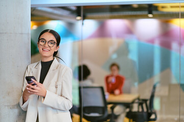 In a modern glass office, a contemporary businesswoman effortlessly multitasks, using her...
