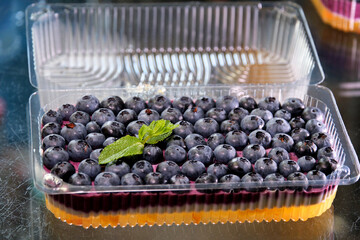 Blueberry jelly from blueberries is poured in a thin stream of delicious healthy dessert with mint leaves in a disposable plastic container delivery of sweets to your home. Healthy homemade food