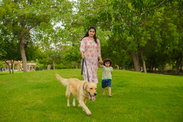 Happy young indian mother and child daughter walking with dog having fun at summer park.