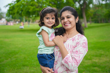 Portrait of happy young indian mother and cute little girl daughter at summer park or garden.