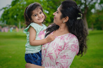 Happy playful young indian mother and cute little girl daughter at summer park or garden.