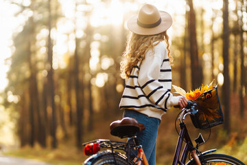 Happy active woman in stylish clothes rides a bicycle in an autumn park at sunset. Outdoor...
