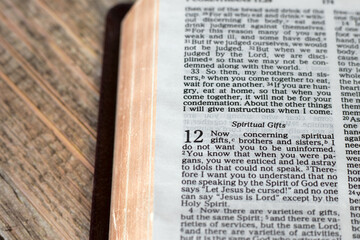 Christian verses about spiritual gifts in open holy bible book with golden pages on wooden table. Close-up.