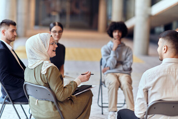 A diverse group of young business entrepreneurs gathered in a circle for a meeting, discussing corporate challenges and innovative solutions within the modern confines of a large corporation