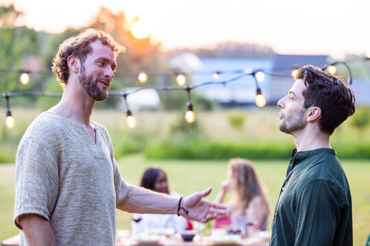 Amidst the vibrant ambiance of a multiracial millennial garden dinner party, two friends engage in an animated conversation. Their laughter and connection are a testament to the bonds of friendship