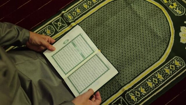 Muslim man reading The Quran holy book on a prayer mat. TRANSLATION of the muslim prayer: "God is the greatest"