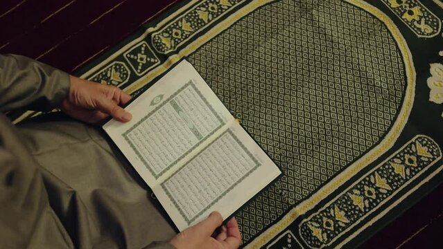 Muslim man reading The Quran holy book on a prayer mat