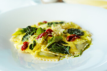 Italian ravioli pasta with basil, spinach, sun-dried tomatoes, pine nuts and cheese in a white plate. Traditional Italian cuisine in the restaurant