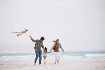Family, running and flying a kite at beach outdoor with fun energy, happiness and love in nature. Man and woman playing with a girl kid on holiday, freedom adventure or vacation at sea with banner