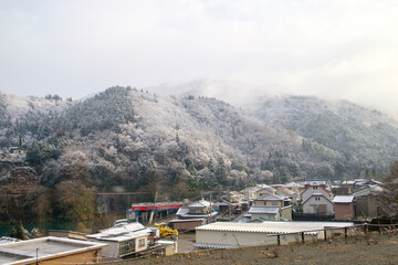 a rural village in Japan during the winter season. This picturesque scene showcases the village nestled among towering snow-capped mountains, creating a breathtaking backdrop of natural splendor.