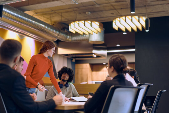 A diverse team of business experts in a modern glass office, attentively listening to a colleague's presentation, fostering collaboration and innovation.