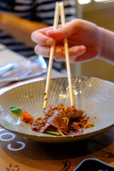 Woman's hand using chopsticks to eat Australian striploin beef spicy Thai salad