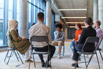 A diverse group of young business entrepreneurs gathered in a circle for a meeting, discussing corporate challenges and innovative solutions within the modern confines of a large corporation