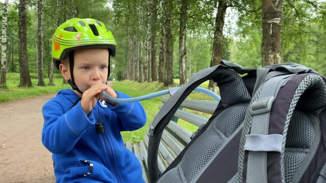 little boy drinking water from hike water system, toddler child in safety helmet with balance bike in park