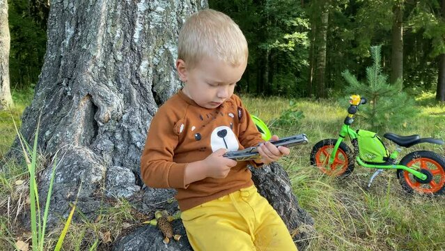 toddler child playing with multitool in summer forest, little boy with balance bike in park
