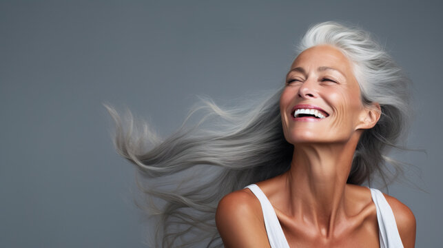 Portrait of smiling beautiful old woman with gray long hair in dynamic motion on grey background