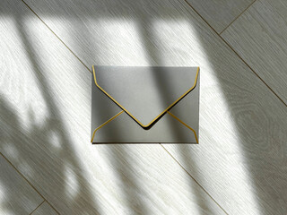 Silver envelope on a light wooden background with shadows from the sun. Flat lay, top view, copy space.