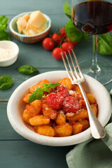Potato gnocchi. Traditional homemade potato gnocchi with tomato sauce, basil and parmesan cheese on turquoise rustic kitchen table background. Traditional Italian food. Top view.
