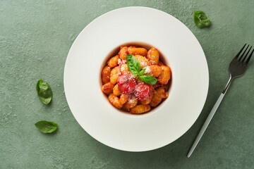 Potato gnocchi. Traditional homemade potato gnocchi with tomato sauce, basil and parmesan cheese on kitchen table on light green kitchen table background. Traditional Italian food. Top view.