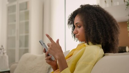Bored African American ethnic woman gadget addict girl chatting online smartphone overuse social media addiction lazy sad female homeowner on cozy sofa at home mobile phone scrolling news on cellphone - Powered by Adobe
