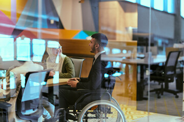 In a modern glass startup office, a wheelchair-bound director leads a successful meeting with...