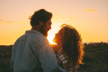 Romantic couple looking each other with love against an orange amazing sunset in outdoor. Romance...