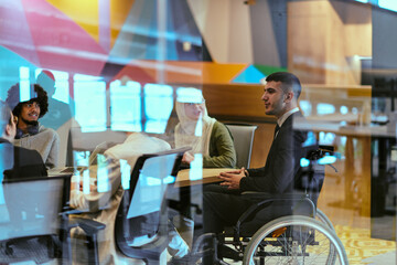 In a modern glass startup office, a wheelchair-bound director leads a successful meeting with...