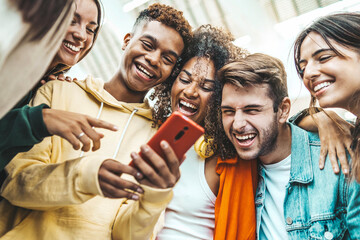 Multiracial young people using smart mobile phone device outdoors - Happy teenagers watching funny reel on smartphone - Technology life style concept - obrazy, fototapety, plakaty