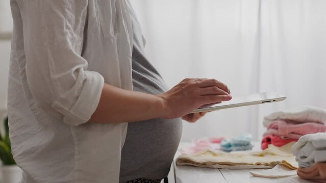 Parent. Caucasian girl in comfortable maternity clothes is preparing for childbirth in a room filled with bright light. Camera in motion, modern mother writes down baby care methods in diary, newborn